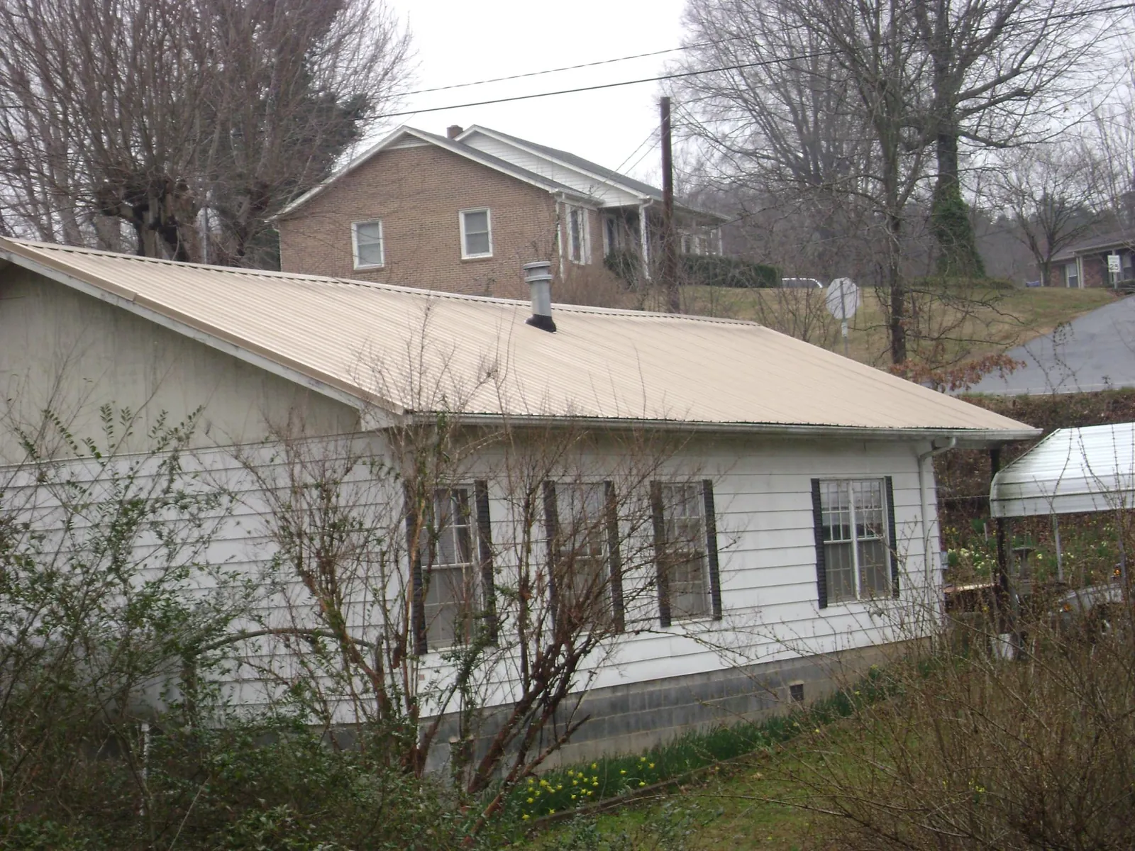 Tan metal roof on a white sided house set into a hillside — Commercial Roofing by Roofing Brothers in Greenfield